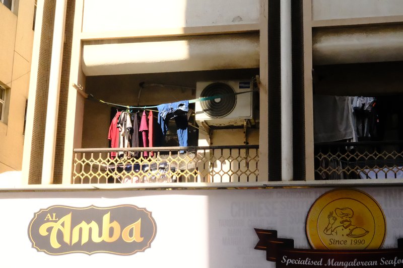 A balcony with clothes hanging to dry, featuring an air conditioning unit and a sign for 'Amba'.