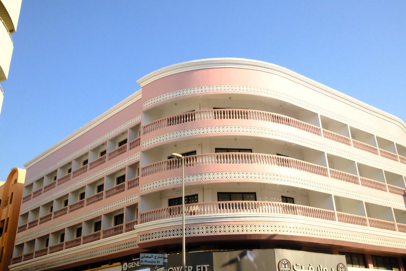 A modern building with a curved facade painted in light pink against a clear blue sky.