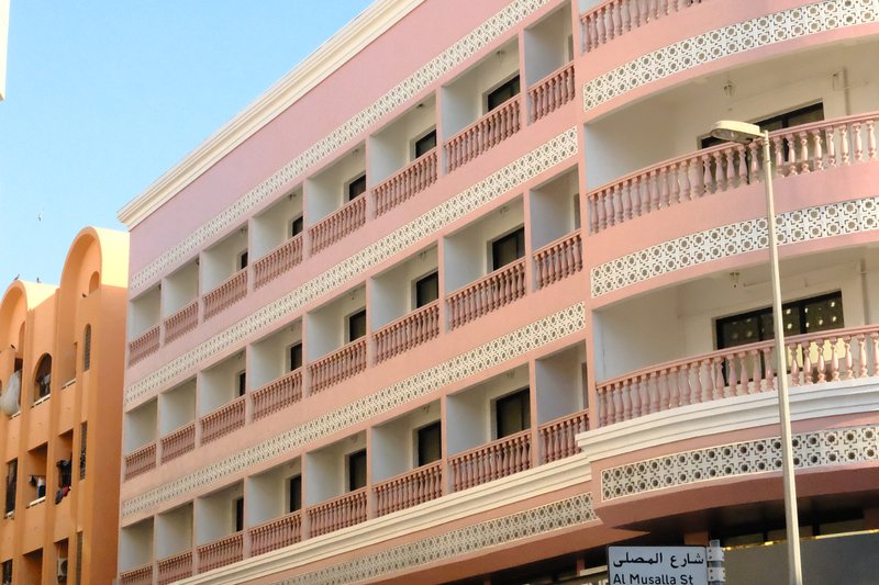 A pink and white building with multiple balconies and windows against a clear blue sky.