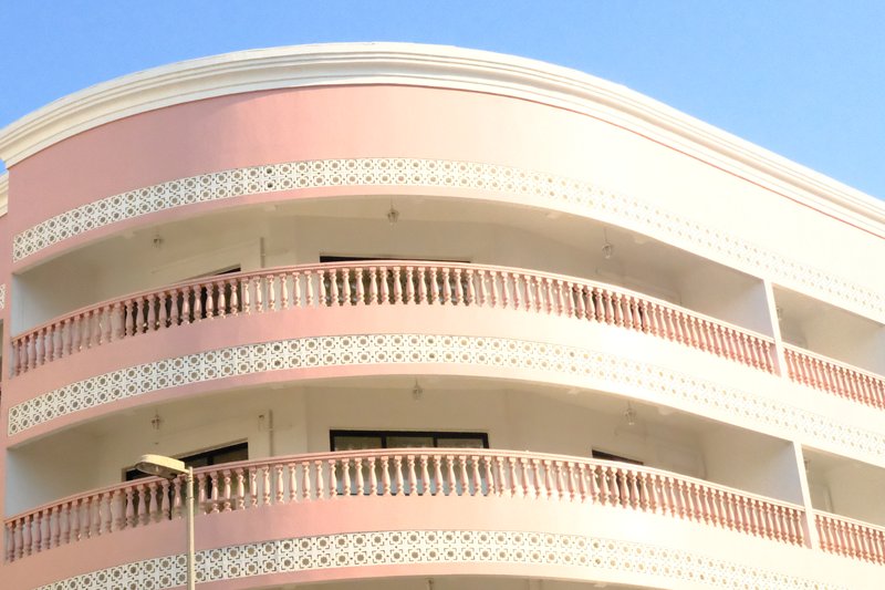 Close-up of a modern building with curved balconies and a pastel pink facade against a clear blue sky.