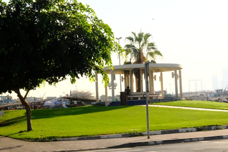 A gazebo surrounded by green grass and palm trees under bright sunlight.
