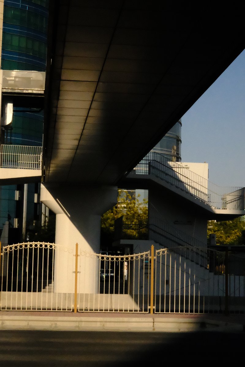 Abstract view of modern architecture with shadows and a fence under a bridge.