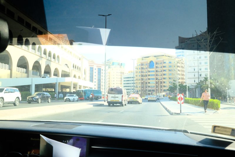 View from a car dashboard showing a city street with buildings and parked cars.