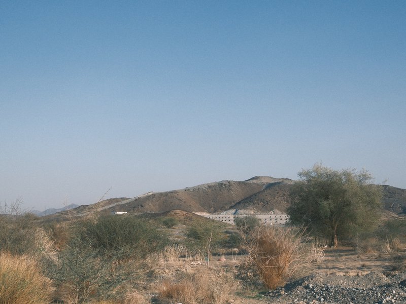 A dry landscape with rolling hills and sparse vegetation under a clear blue sky.