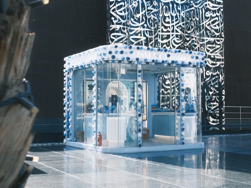 A small blue and white kiosk with decorative elements, surrounded by reflective surfaces and modern architecture.