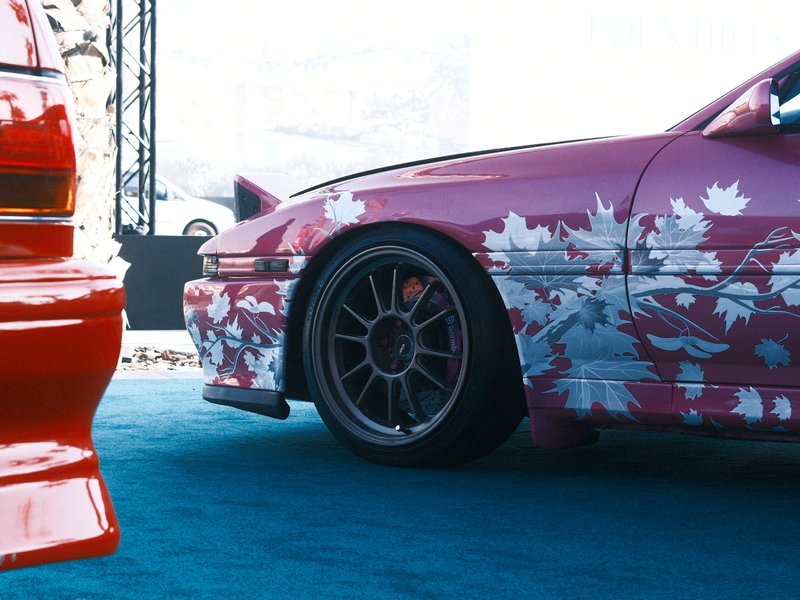 Close-up of two modified cars, one pink with floral designs and one red, on a blue surface.