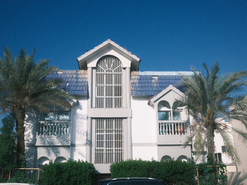 A modern two-story house with palm trees in front and a clear blue sky.