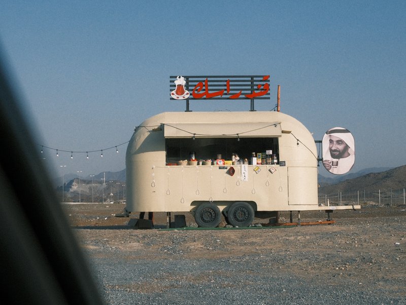 A vintage food trailer in a rural setting with a clear blue sky and mountains in the background.