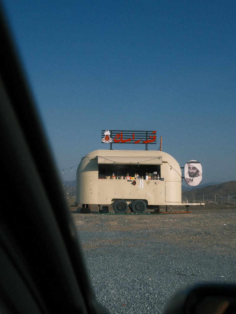 A food truck with a rounded structure set against a clear blue sky, viewed from a car window.
