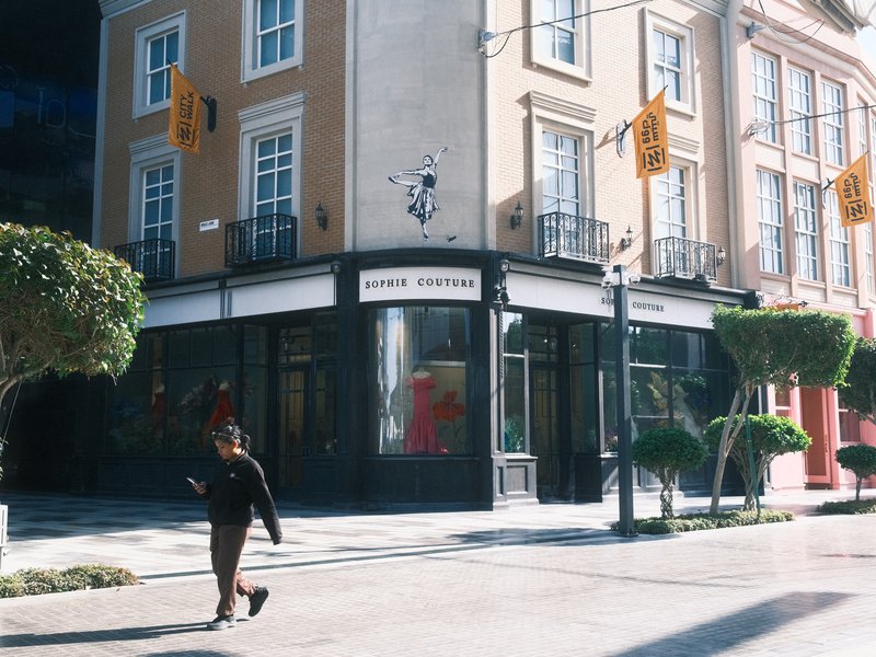 A woman walking past a stylish storefront in an urban setting with trees and decorative elements.