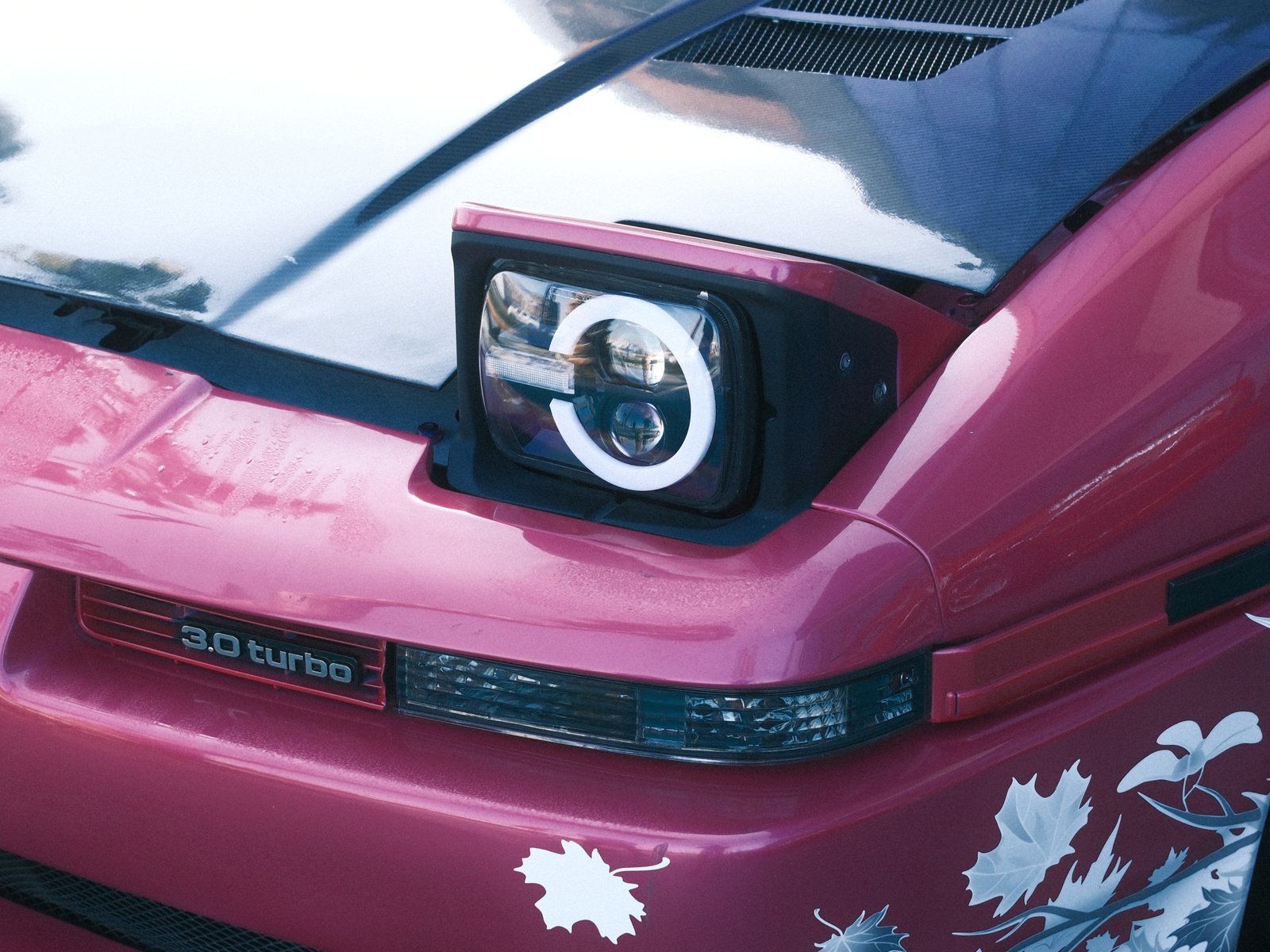 Close-up of a pink sports car's headlight and hood with floral designs.