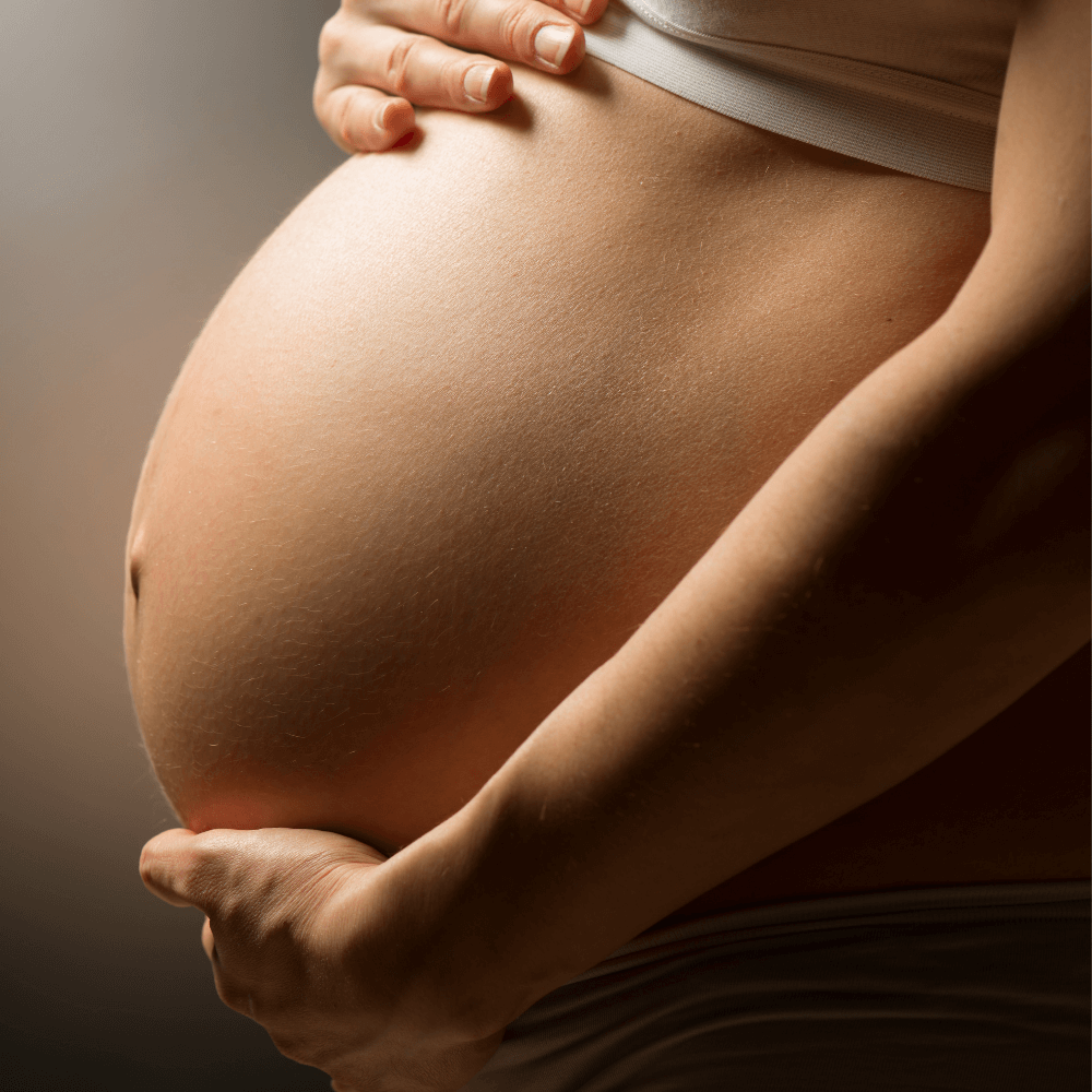 Close-up of a pregnant woman's belly with hands gently resting on top and bottom