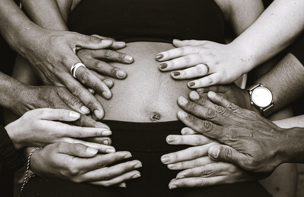 Multiple hands of diverse people gently touching a pregnant belly, symbolizing support and community