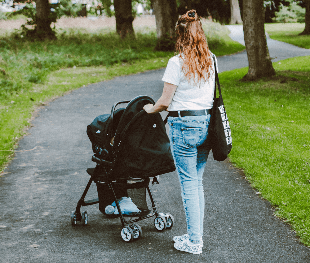Nanny walking with a stroller on a park path during childcare duties