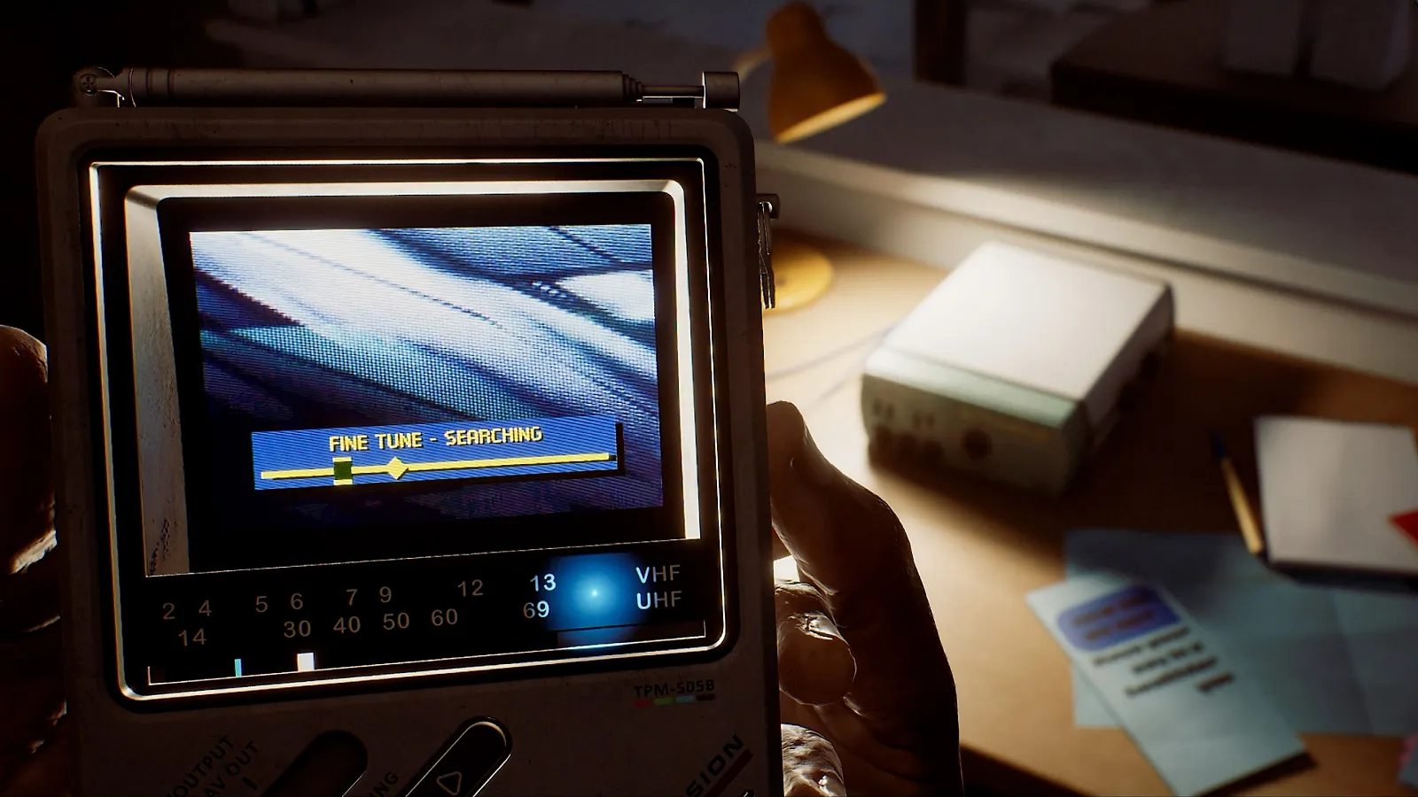 Simon holding the CRTV pocket television while examining an object on a desk in Silent Hill Townfall