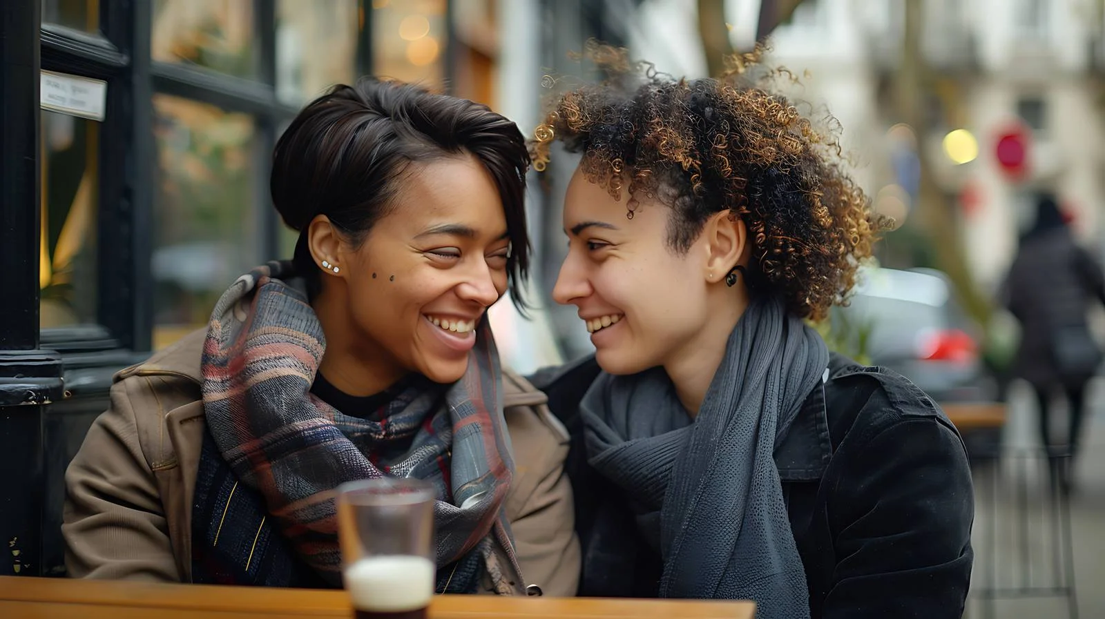 Joyful lesbian couple at urban sidewalk cafe — free download from Dotvec