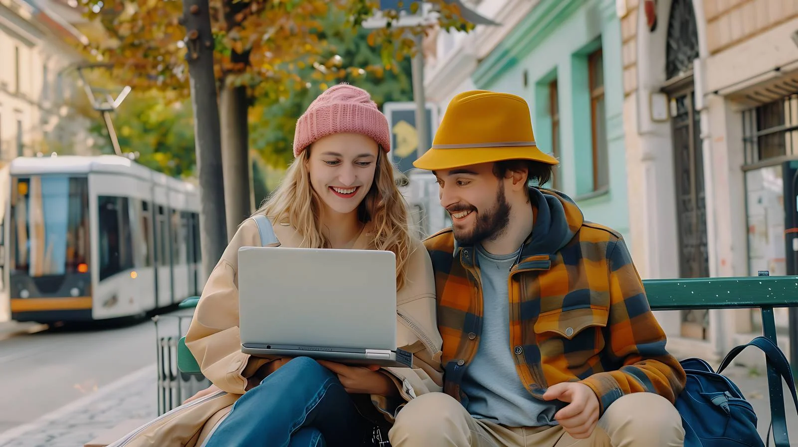 Joyful couple working on laptop at tram stop — free download from Dotvec