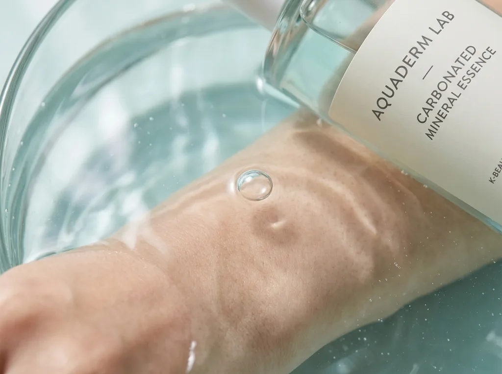 The intimate, almost scientific beauty of carbonated water meeting skin not a spa advertisement, but a biology lesson made visible The water is crystal-clear with a faint mineral blue-green tint One bubble detaches, mid-ascent