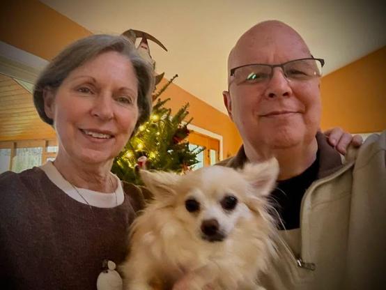 Head and shoulders shot of woman on left, longhaired chihuahua in middle and man on right. 