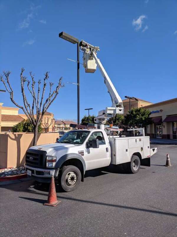 An electrician services a parking lot light from a cherry picker attached to a Ford F-450 truck.