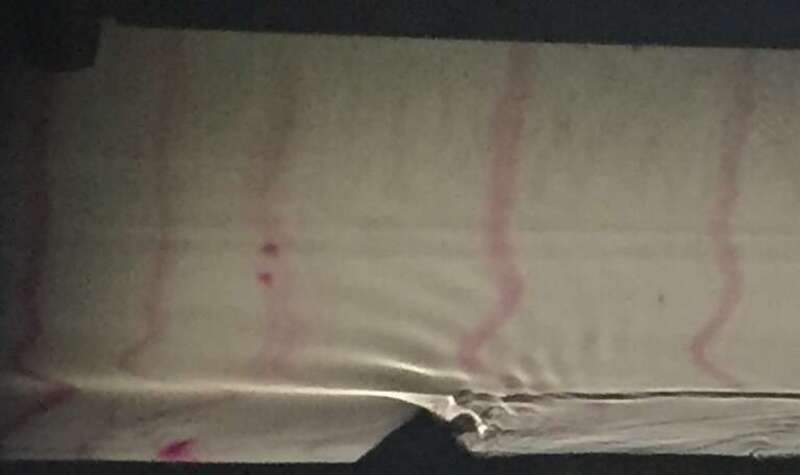 A fluid dynamics lab experiment illustrates flow past a mountain-shaped obstacle. Downstream wave crests radiate upwards with their group velocity pointing about 45° from horizontal. A downslope jet can be seen in the lee of the mountain, an area of