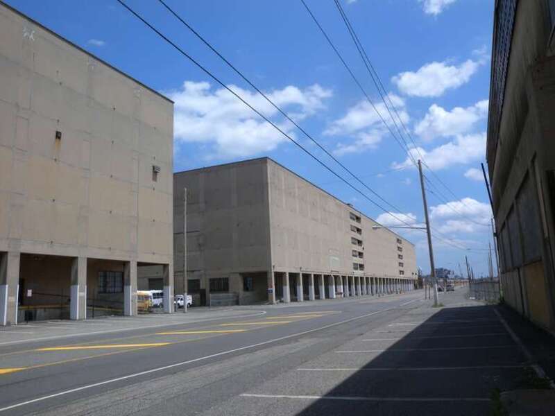 Looking east between warehouses on a hazy midday.  File:Bayonne Drydock &amp; Repair jeh.jpg is in distant background.