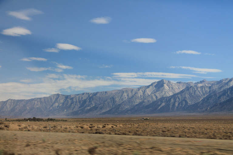 
500px provided description: Mountains From The Highway We Re Almost There [#sky ,#mountains ,#blue ,#white ,#plains]