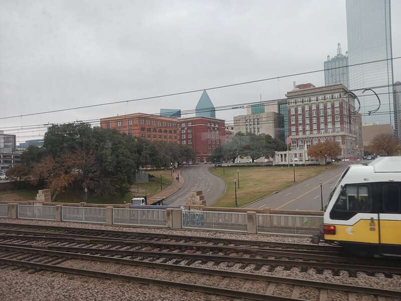 Looking northeast along Elm St. in Dallas, toward the Texas School Book Depository (orange brick building, our Object Location below) from the Amtrak Texas Eagle train on the Triple Overpass. Here we faintly also see the X's on the pavement marking
