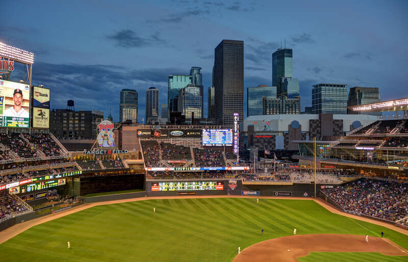 The Minneapolis skyline behind the field and stands of Target Field during an evening baseball game.