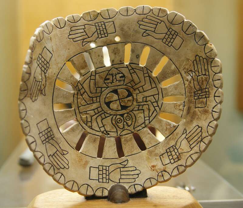 Spiro mound artifacts on display at Woolaroc Museum, near Bartlesville. Spider motif at center with circle of hands with shell bracelets. Roughly 3 in x 3 in.
