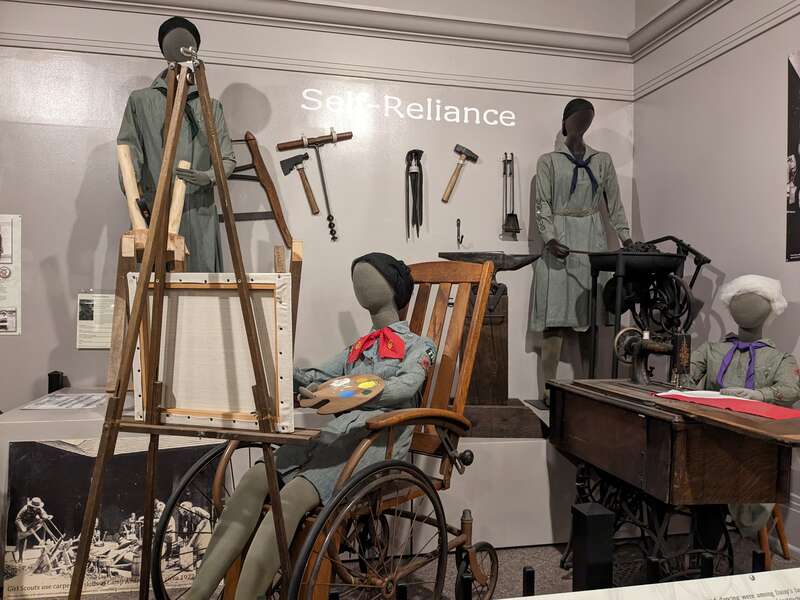 A display of vintage uniforms and equipment related to the Girl Scouts of America