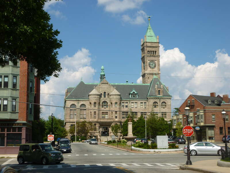 Lowell City Hall, located at 375 Merrimack Street Lowell, Massachusetts.  Southwest side of building shown.  Visible in the foreground is a raised island containing monuments to the city's early Greek immigrants, Cardinal O'Connell, and the city's
