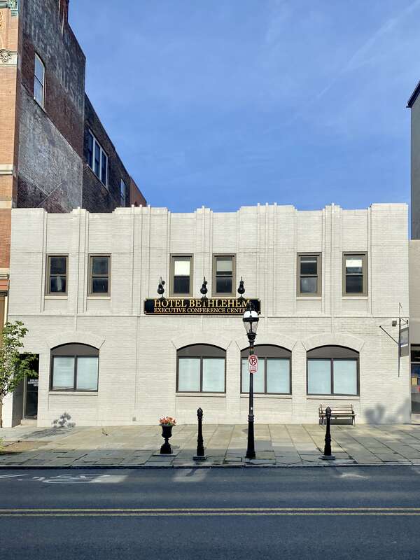 Built in the early 20th Century, this Art Deco-style building features a painted brick exterior, pilasters that stair-step in and out of the facade with vertical lines of single bricks in the middle of each pilaster except at the ends, recessed