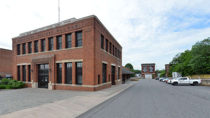 he two story Chesapeake Western Railway station on the left is now being used as offices. On the right is the side of the Rockingham Milling Company building with an advertisement originally dating from the 1920s painted on it. Further right, across
