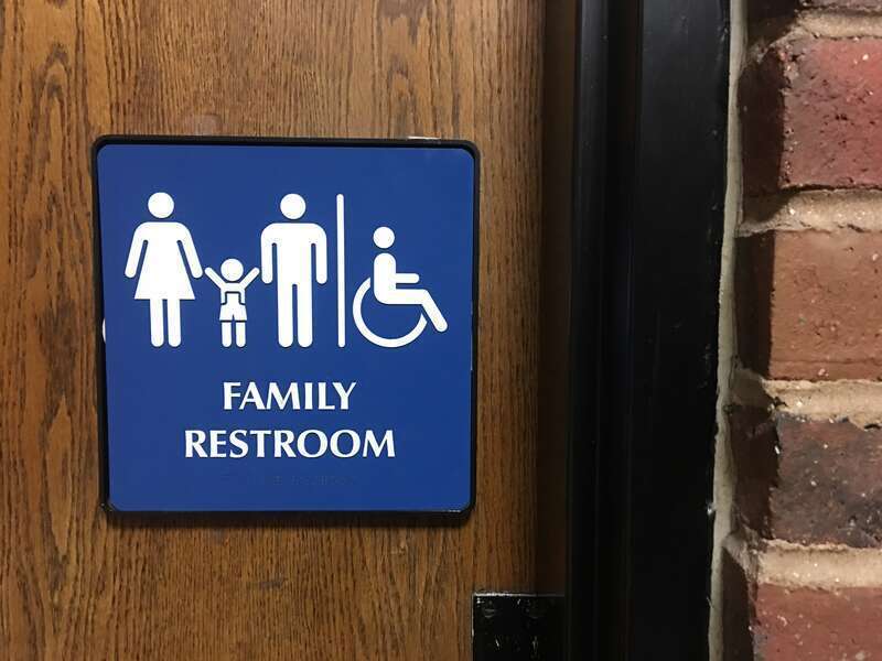 A sign indicating a gender-inclusive, children &amp; family, ADA compliant restroom at a public library in Nashua, New Hampshire