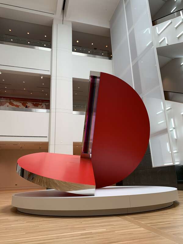 Image of a sculpture titled "Folded Circle Dynamics Red Phase III" by Fletcher Benton on display in the main hall of the Indianapolis Museum of Art at Newfields