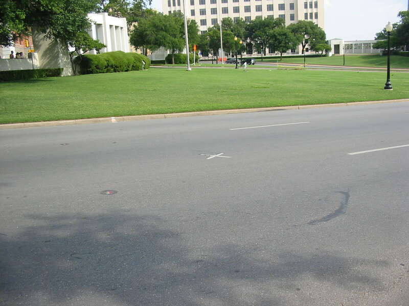 Looking south across Dealey Plaza. Elm Street is in the foreground, with Main Street and Commerce Street in the background. The presidential motorcade traveled down Elm Street from left to right. An X on the street marks the position of JFK during