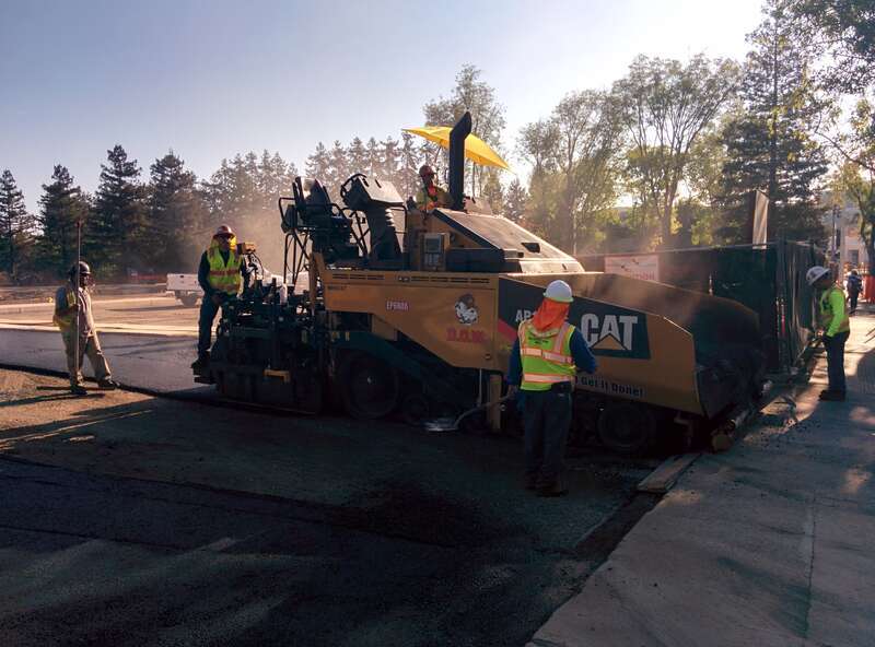 A crew operates a paving machine in the parking lot of an Apple building in Cupertino, California.