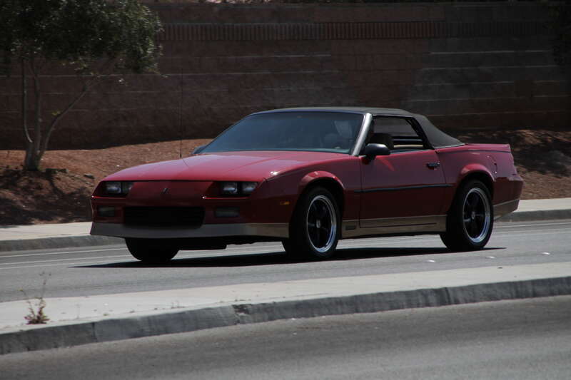 A red 1987-92 Chevrolet Camaro Convertible driving in the northbound lanes of North Jones Boulevard, Las Vegas, Nevada.