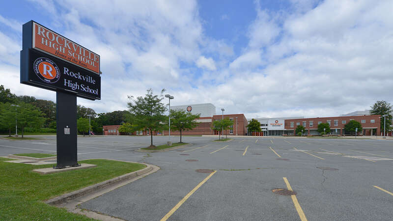 The sign along the road for Rockville High School with a parking lot and the building in the background, part of the Montgomery County Public Schools system. 2100 Baltimore Road, Rockville, Maryland 20851.