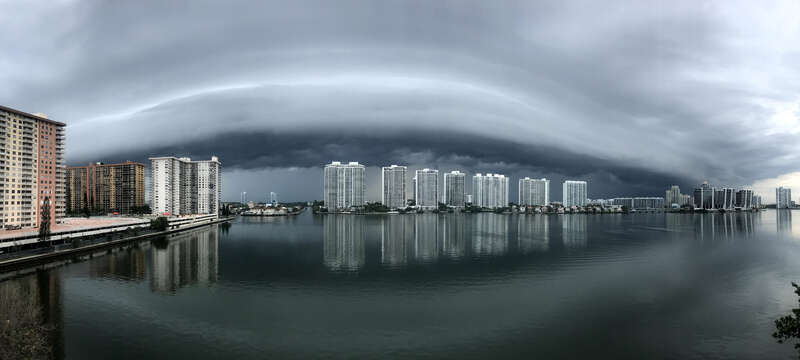A shelf cloud (a type of arcus cloud) reflecting on Dumfoundling Bay in northeastern Miami-Dade County, Florida. Apartment buildings in Aventura, Florida are visible on the other side of the bay.