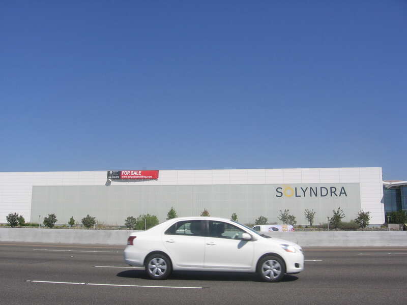 A large factory building owned by Solyndra in Fremont, California, USA with a "For Sale" sign on it.  View is from the shoulder of the southbound side of Interstate 880 (Nimitz Freeway).