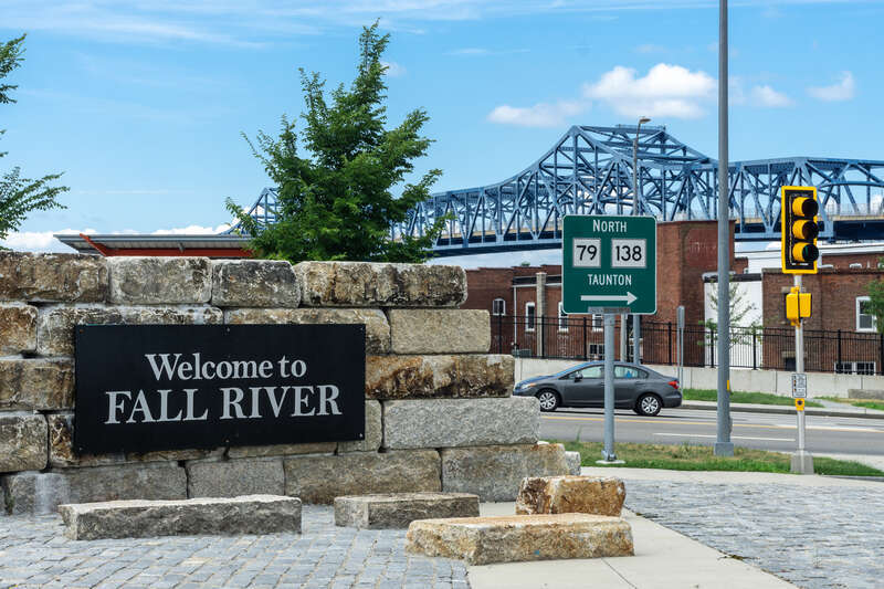 Sign says "Welcome to Fall River" with the Braga Bridge behind it.
