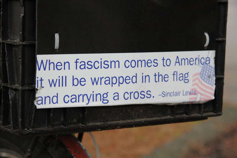 Closeup of bumper sticker with famous Sinclair Lewis line "When fascism comes to America it will be wrapped in the flag and carrying a cross"

This quote is often attributed to Sinclair Lewis but has not been verified. The Sinclair Lewis Society