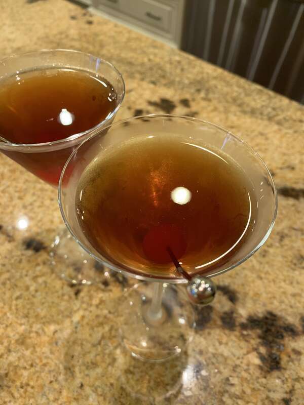Two manhattan cocktails with a maraschino cherry garnish. Bird's eye angle. Granite countertop.