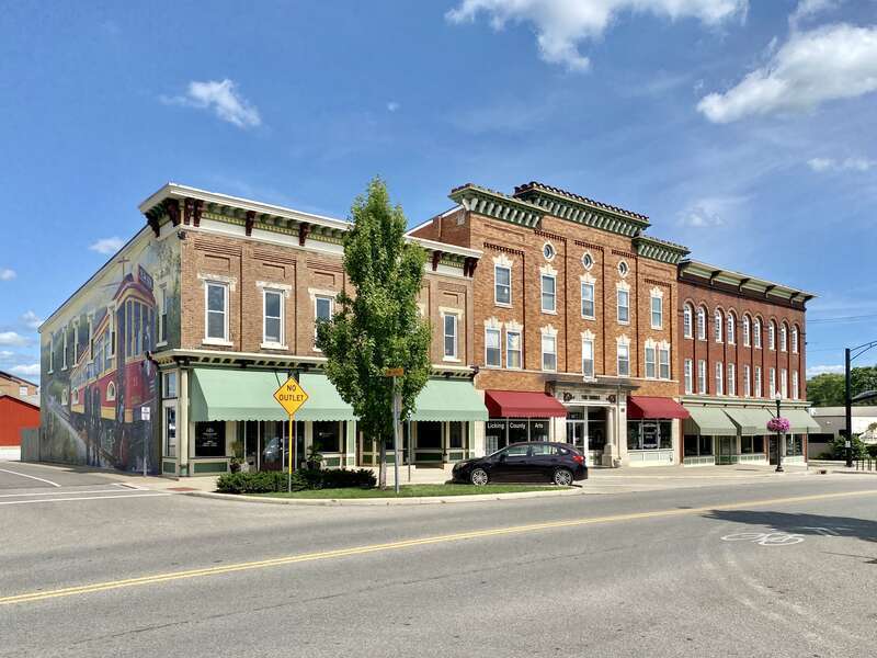 On the left, built in the late 19th Century, this Italianate-style building features a red brick facade with a bracketed cornice featuring modillions and dentils, stone lintels and sills, pilasters between the window bays with recessed brick panels