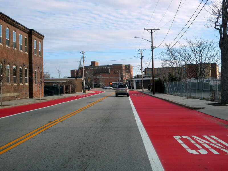 Red-painted bus lanes on Goff Avenue in Pawtucket, seen in December 2022. The lanes were added in 2022 to support RIPTA bus service to Pawtucket/Central Falls station, which opened in January 2023.