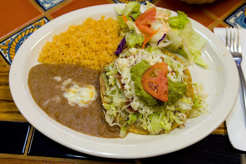 A beef tostada on a plate with refried beans, rice, and a salad as served by Los Compadres Mexican Restaurant at 944 C Street in Hayward, California, USA.  The photographer describes the scene as: "A crispy flat corn tortilla shell topped with beef,