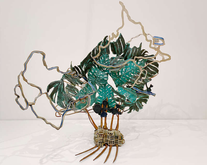 Polychrome bronze (Fayum, 1981) by American artist Nancy Graves on display at the San Francisco Museum of Modern Art with lush green leaves of a monstera plant, meandering cartographic lines and perforated blue abstractions from topographic maps of