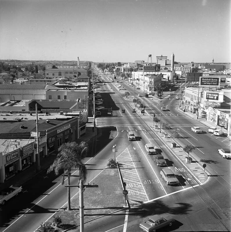 Original caption:  "DOWNTOWN INTERSECTION—Contrasting views of Culver and Washington Blvds., junction looking to the southwest, shows progress of last 40 years." Culver Blvd. is the main thoroughfare and Washington Blvd. is the smaller one.